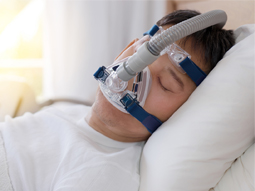 Sleep apnea therapy, man sleeping in bed wearing CPAP mask